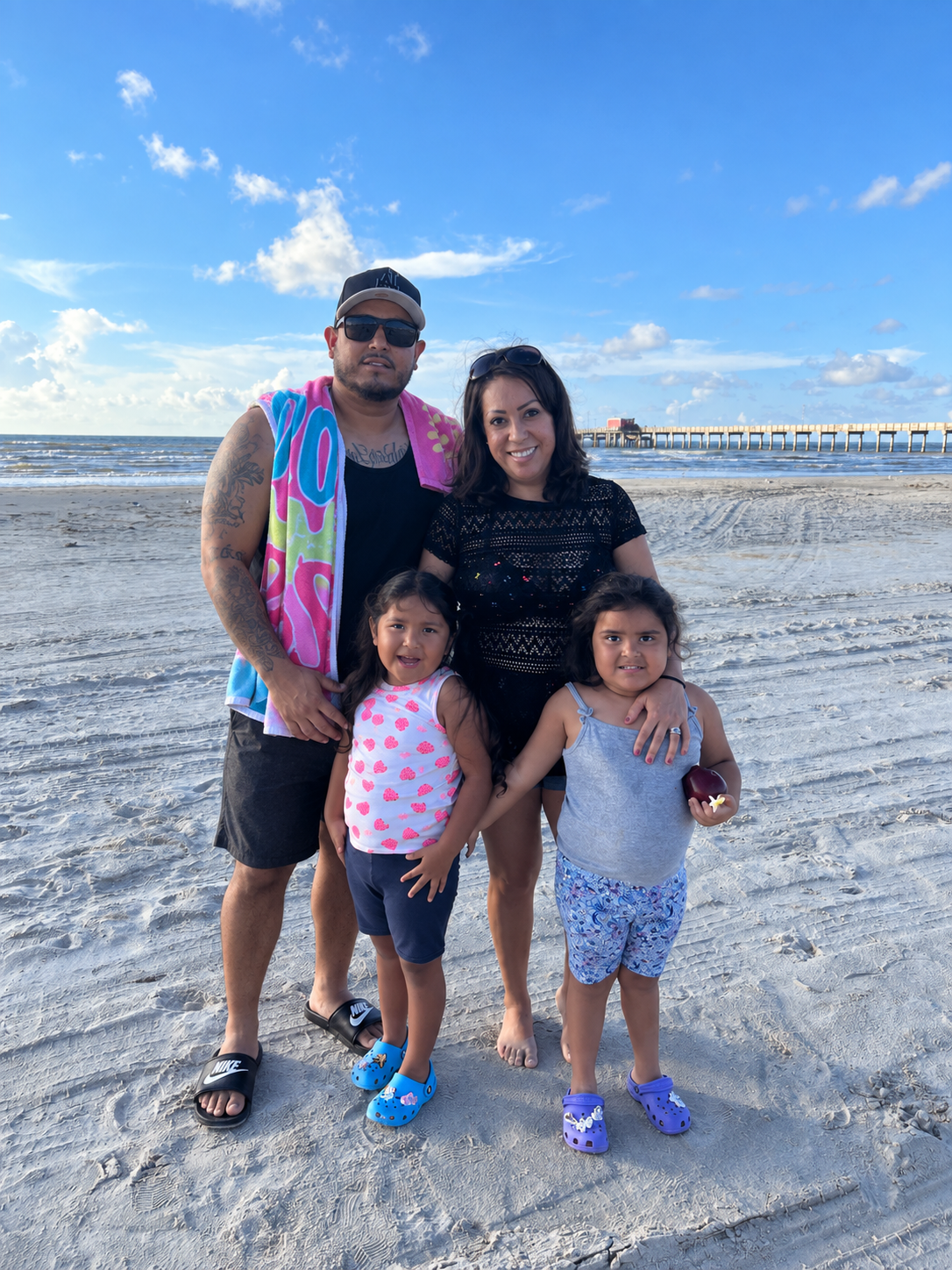 Fernando and his family — wife and two daughters — smiling together on the beach